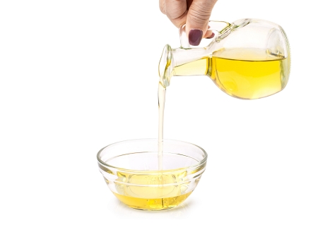 Woman hand hold bottle of extra virgin oil pouring in to glass bowl isolated on white background.